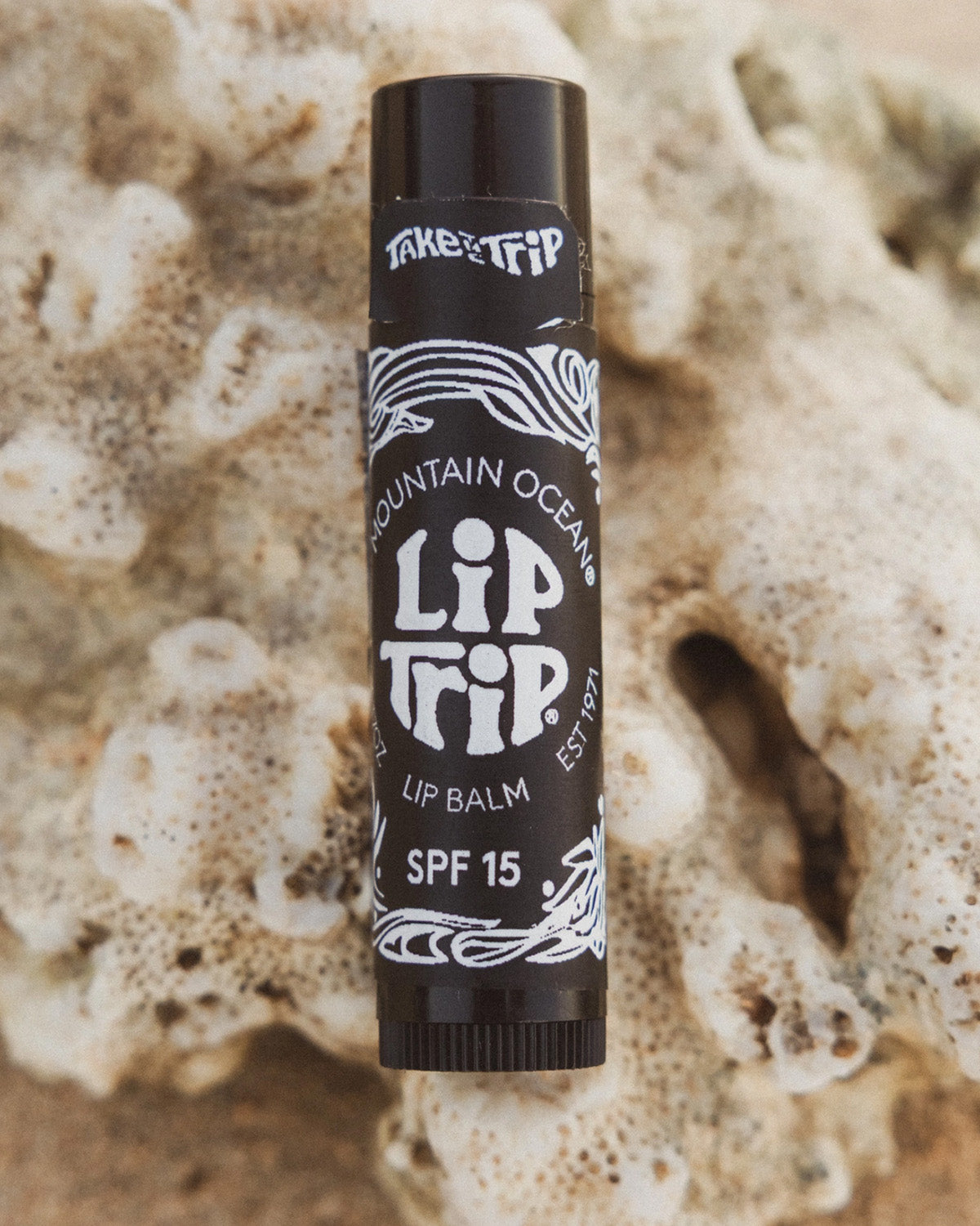 Lip balm stick with 'Lip Trip' branding on a textured beige background
