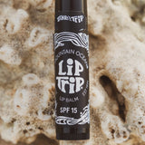 Lip balm stick with 'Lip Trip' branding on a textured beige background