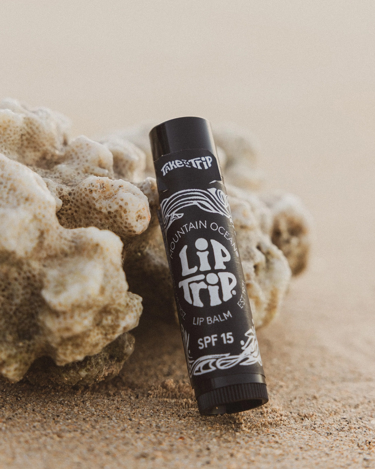 Lip balm stick with 'Lip Tip' branding on a sandy background