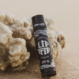 Lip balm stick with 'Lip Tip' branding on a sandy background