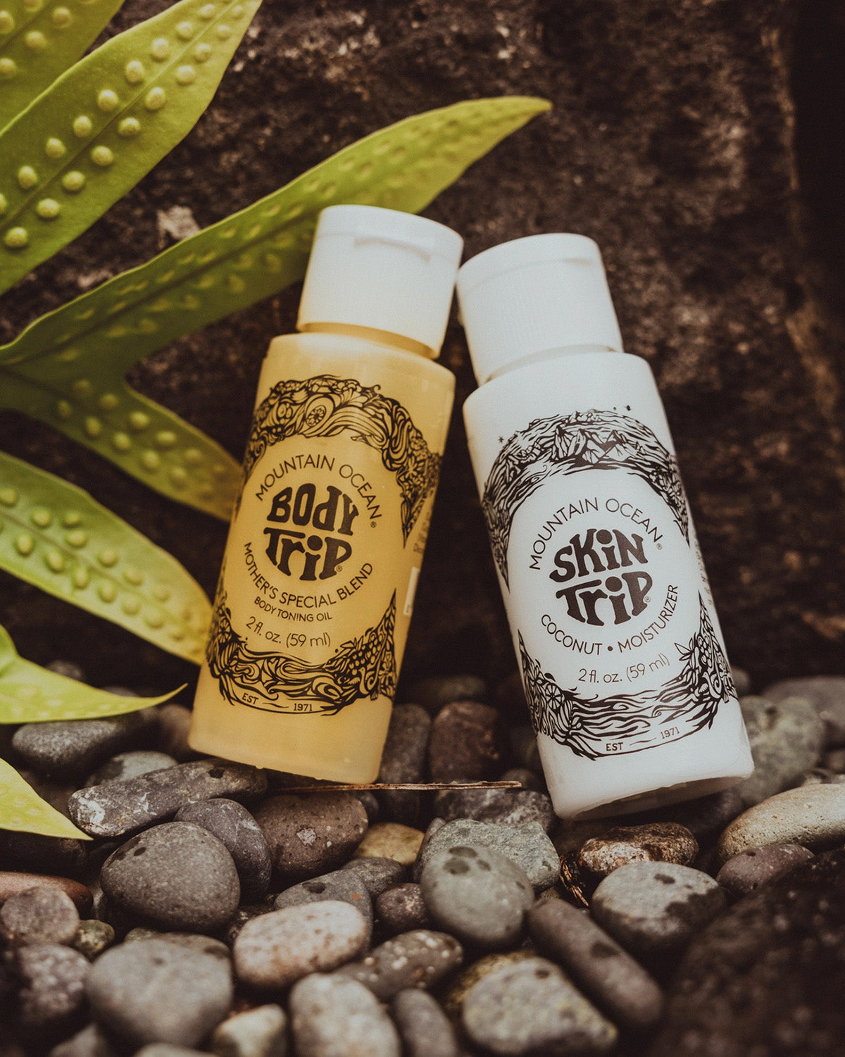Two bottles of Mountain Ocean body and skin care products on pebbles with a leaf in the background