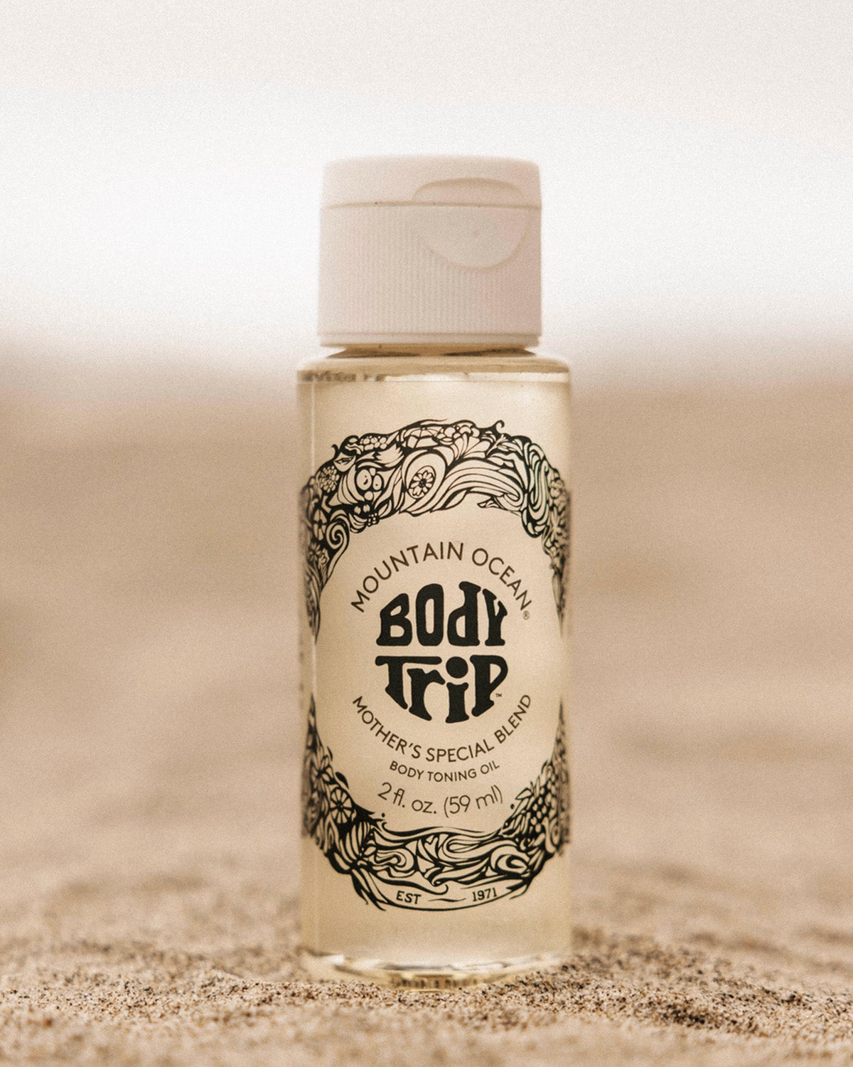 Bottle of Mountain Ocean Body Trip Mother's Special Blend body toning oil on a sandy background