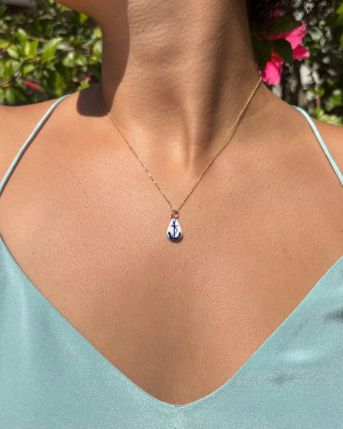 Necklace with a blue pendant worn by a person in a light blue top, with greenery in the background.