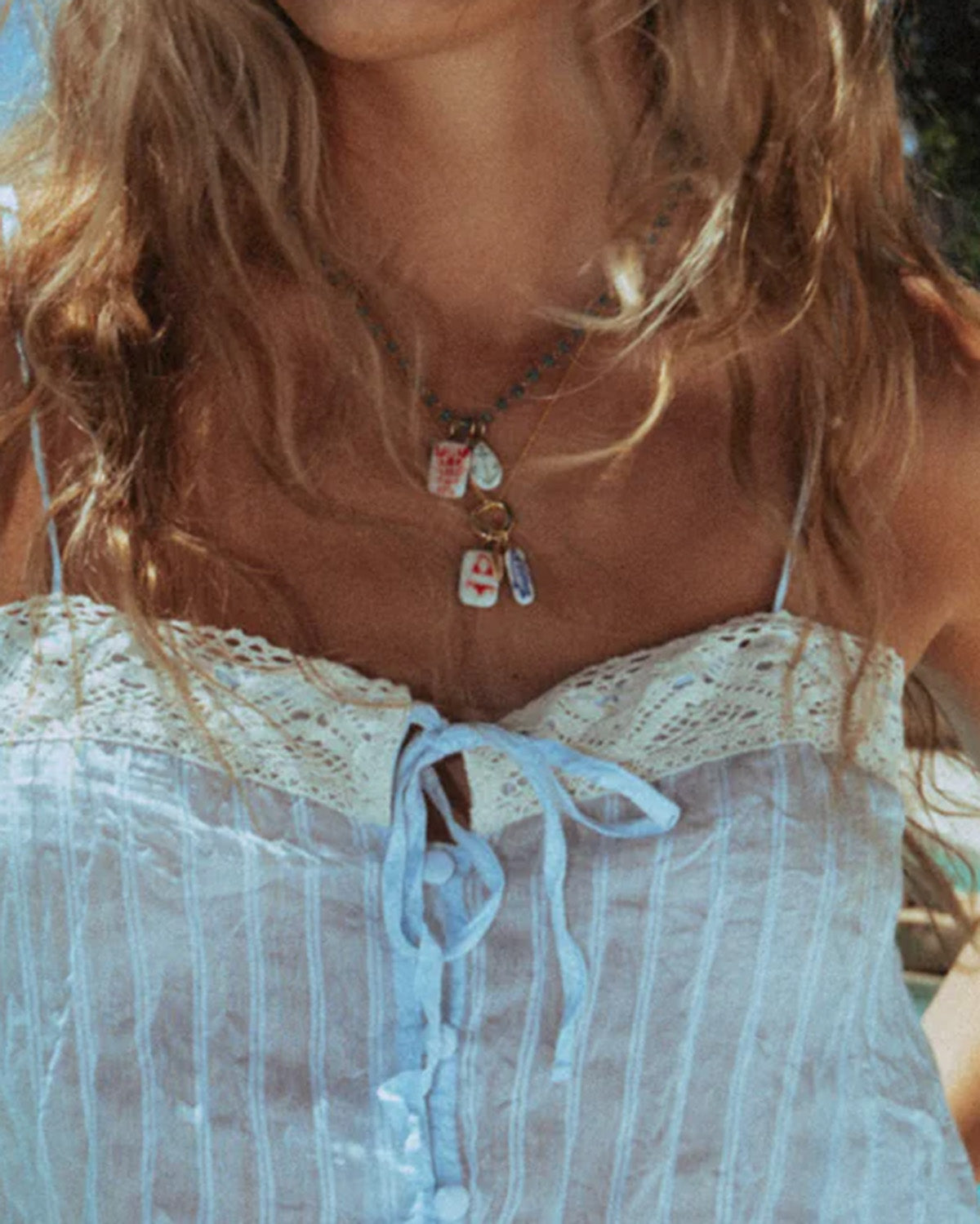 Close-up of a person wearing a white lace top and a necklace with multiple pendants