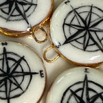 White ceramic charms with black compass designs and gold accents