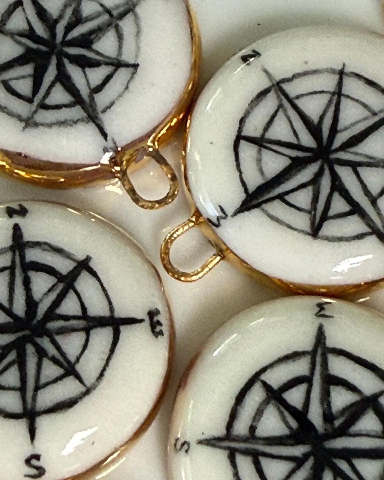 White ceramic charms with black compass designs and gold accents