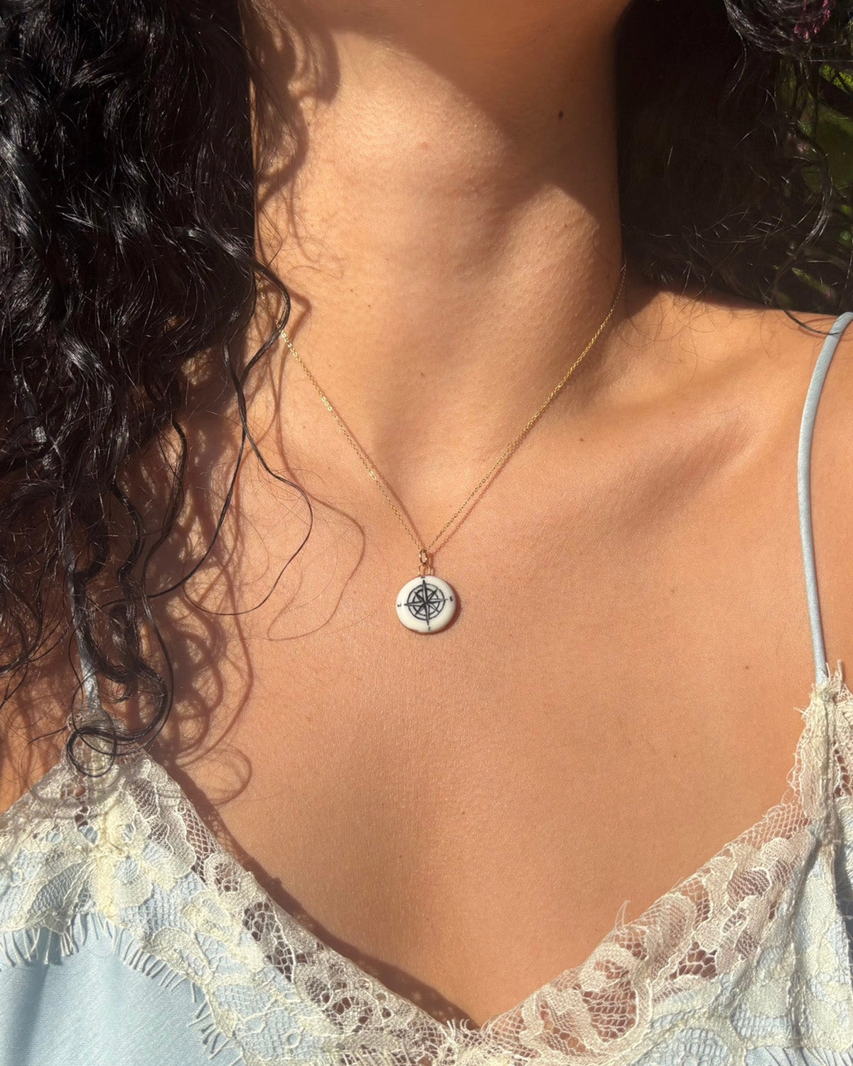 Close-up of a necklace with a pendant on a person wearing a light blue lace top