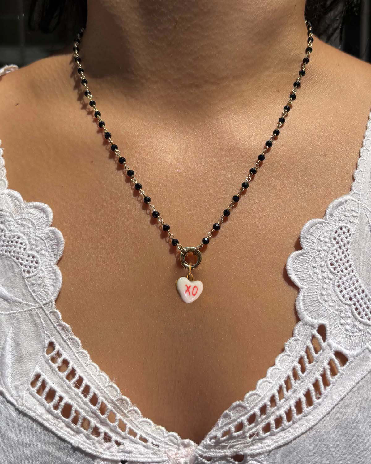 Necklace with a heart-shaped pendant worn by a person in a white lace top.