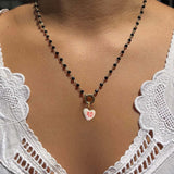 Necklace with a heart-shaped pendant worn by a person in a white lace top.