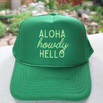 Green cap with 'Aloha howdy HELLO' text on a blurred natural background