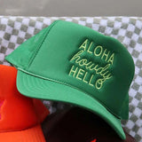 Green cap with 'Aloha howdy HELLO' text on a checkered surface