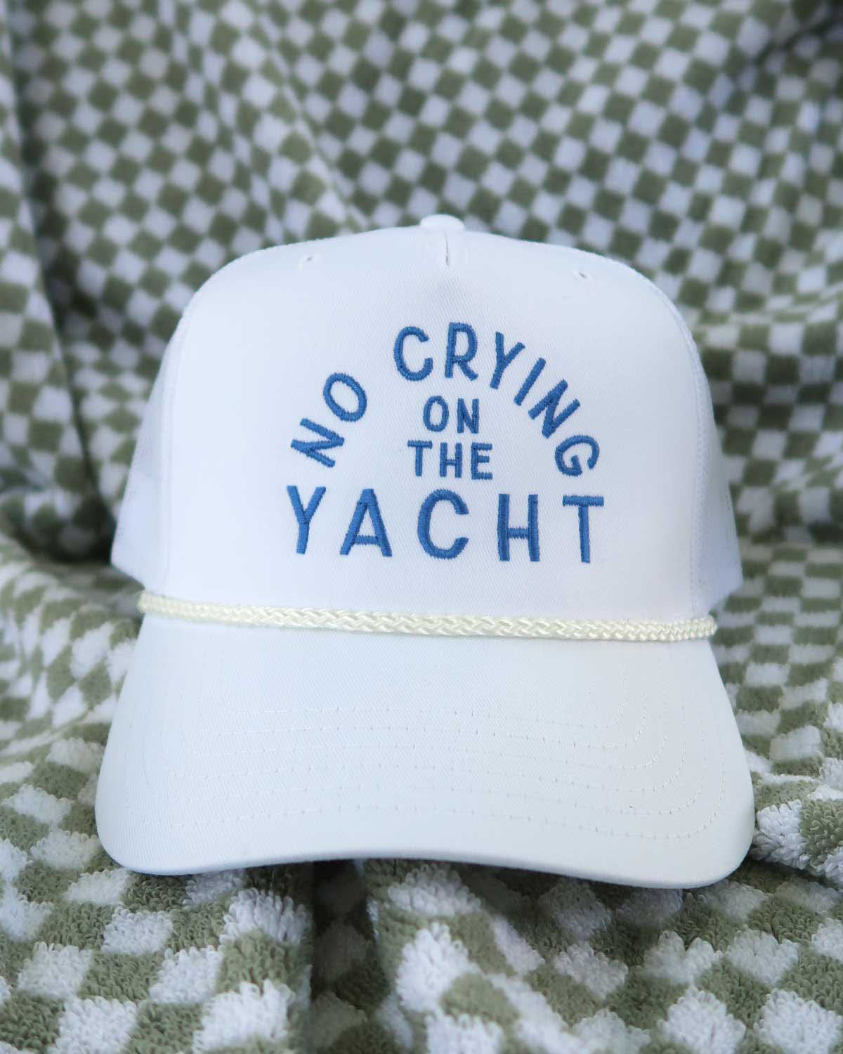 White cap with 'No Crying on the Yacht' text on a checkered fabric background