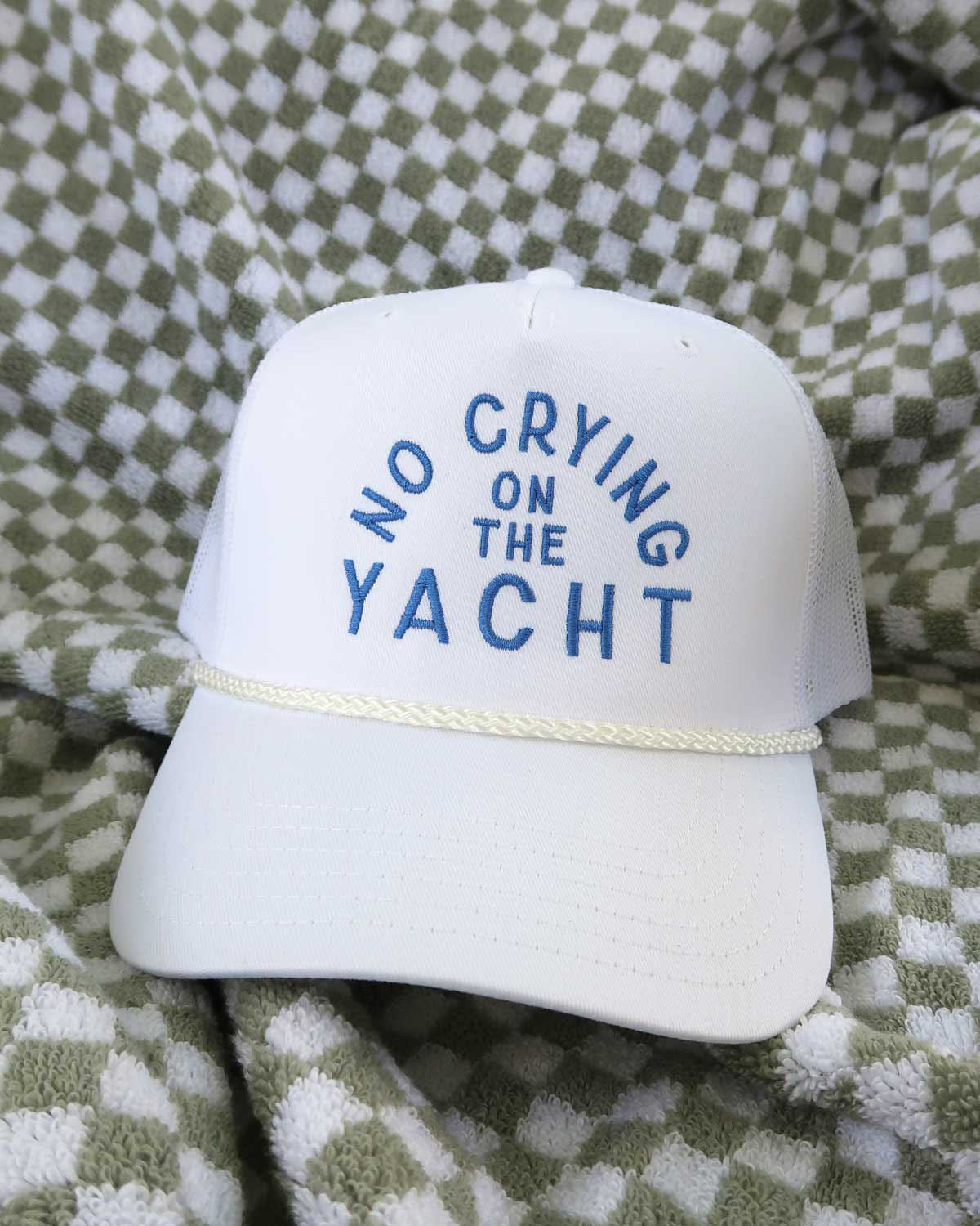 White cap with 'No Crying on the Yacht' text on a checkered fabric background
