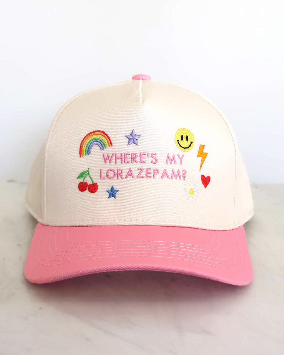 Beige cap with pink visor featuring colorful graphics and text on a light background