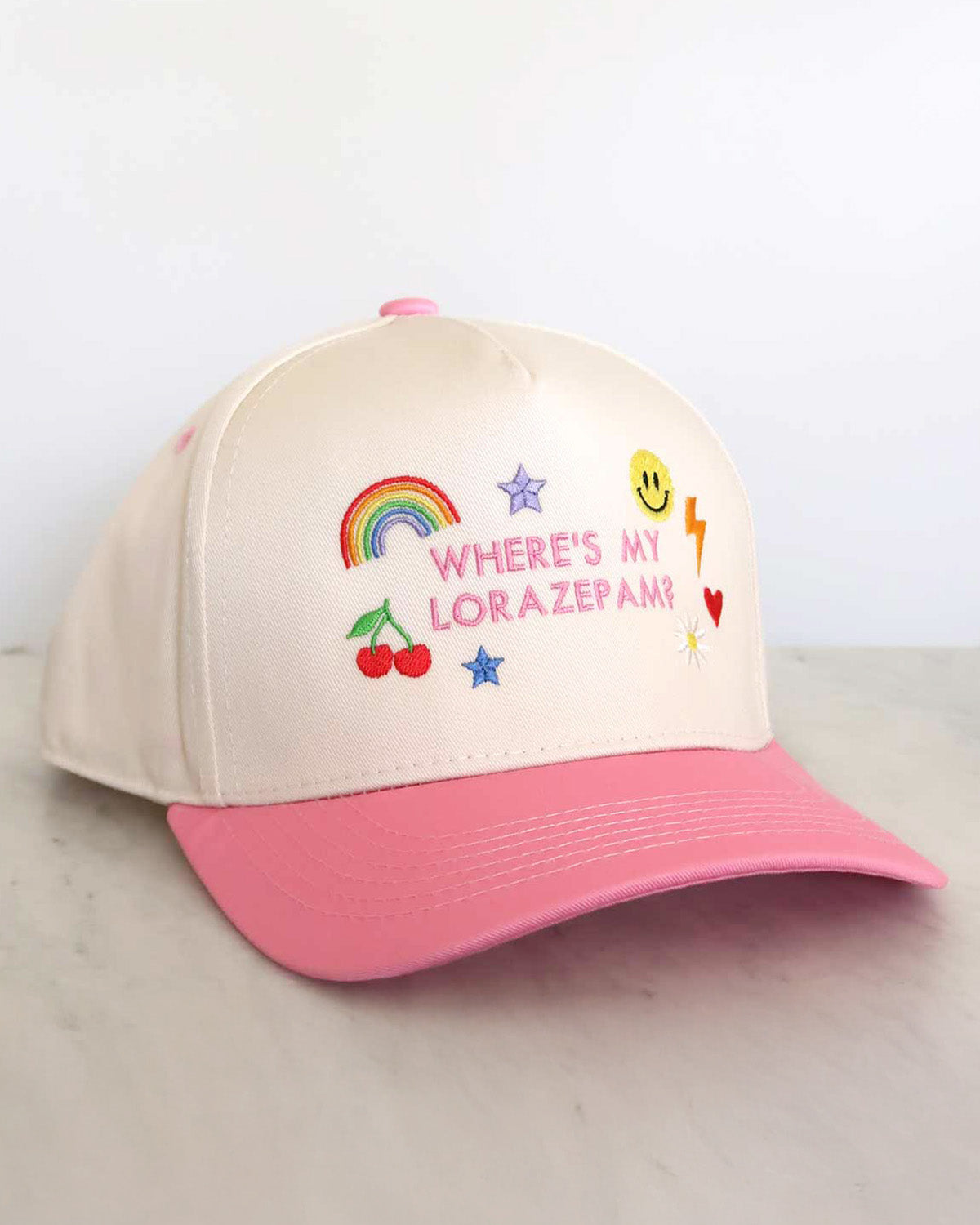 Beige and pink cap with colorful text and graphics on a light gray surface