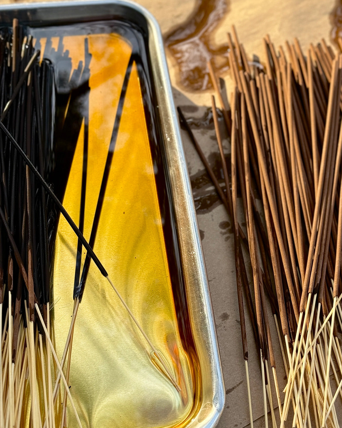 Incense sticks with a tray of melted wax or resin on a reflective surface