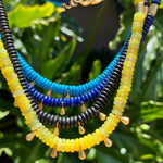 Necklace with blue, yellow, and black beads on a green leafy background