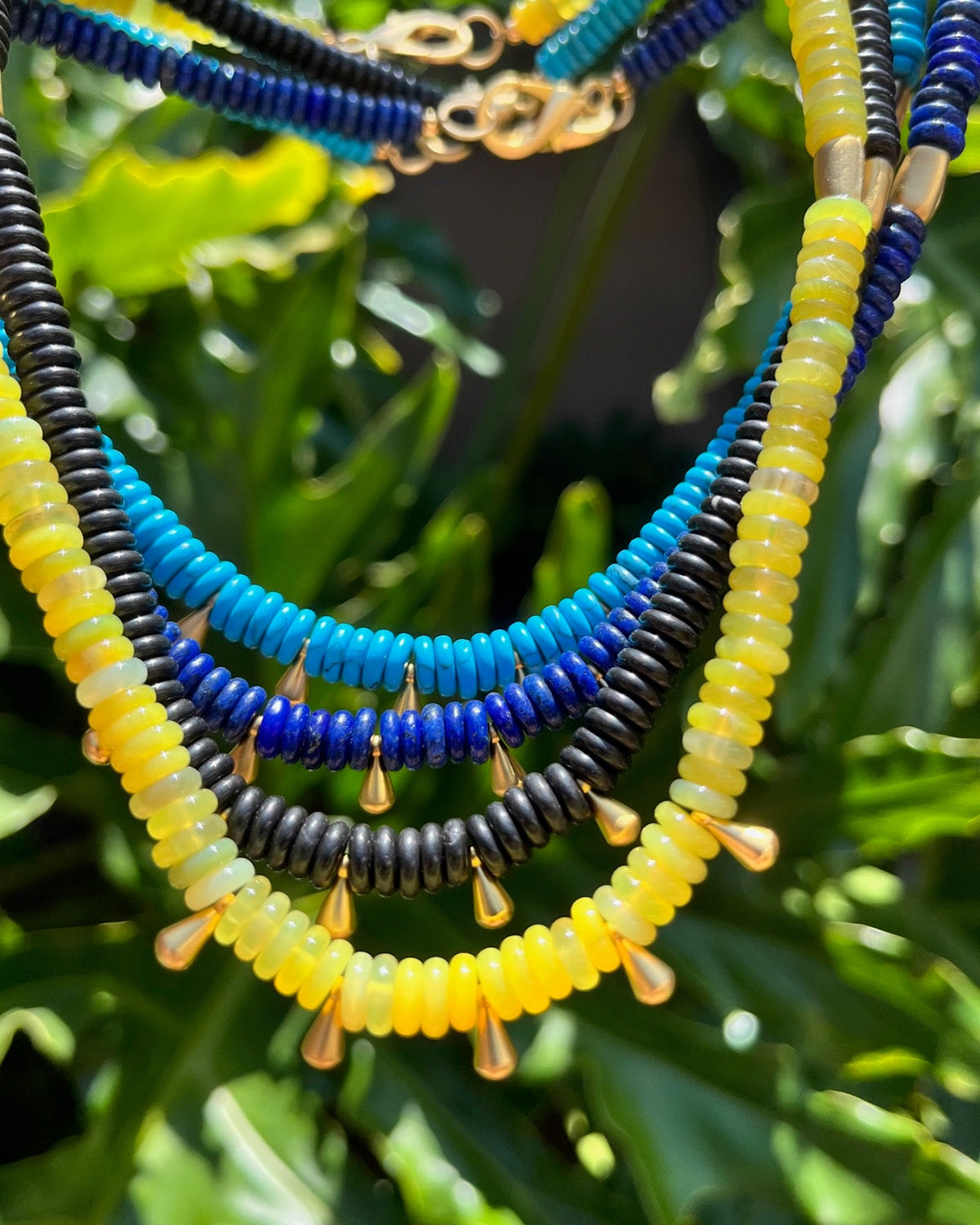 Necklace with blue, yellow, and black beads on a green leafy background