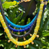 Necklace with blue, yellow, and black beads on a green leafy background