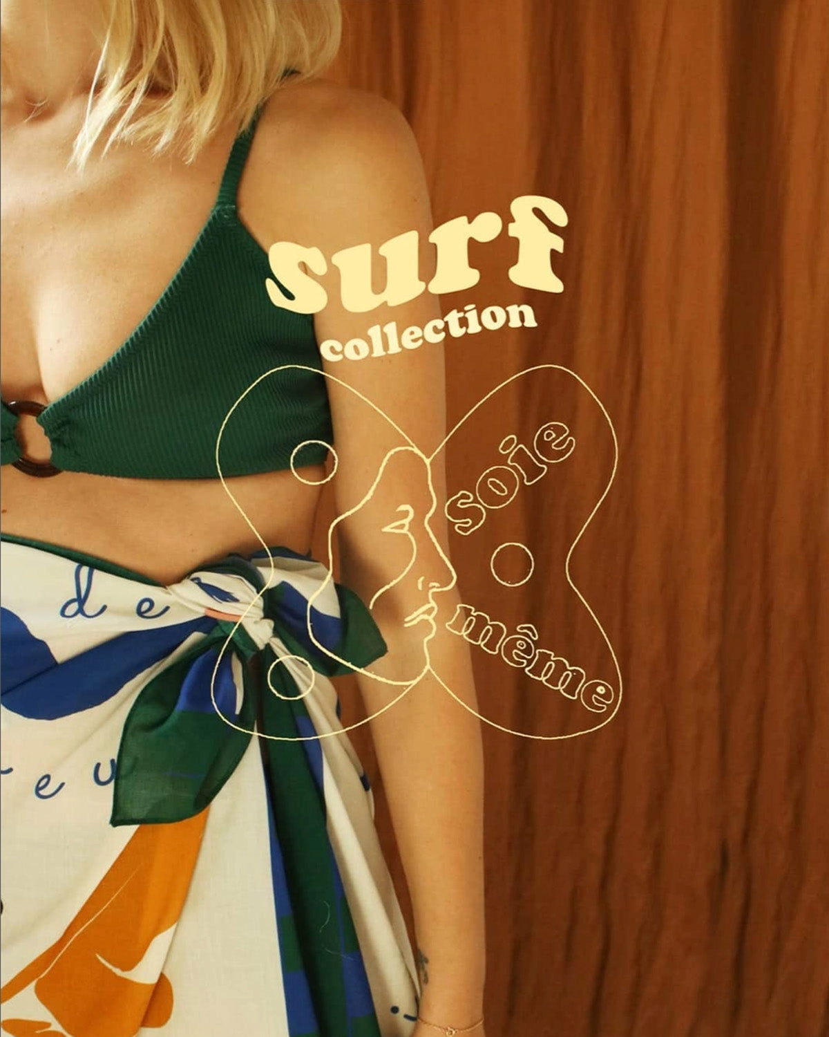 Woman wearing a green bikini top and colorful sarong with 'surf collection' text on a wooden background