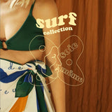 Woman wearing a green bikini top and colorful sarong with 'surf collection' text on a wooden background