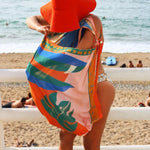 Person on a beach wearing a colorful sarong and red hat