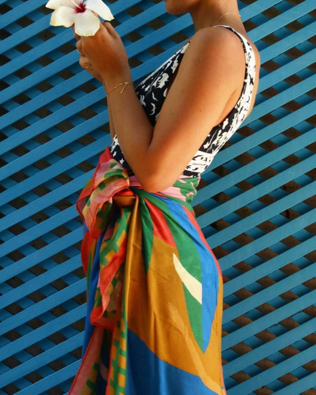 Person wearing a colorful sarong over a black and white patterned top against a blue lattice background