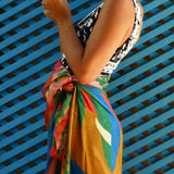 Person wearing a colorful sarong over a black and white patterned top against a blue lattice background