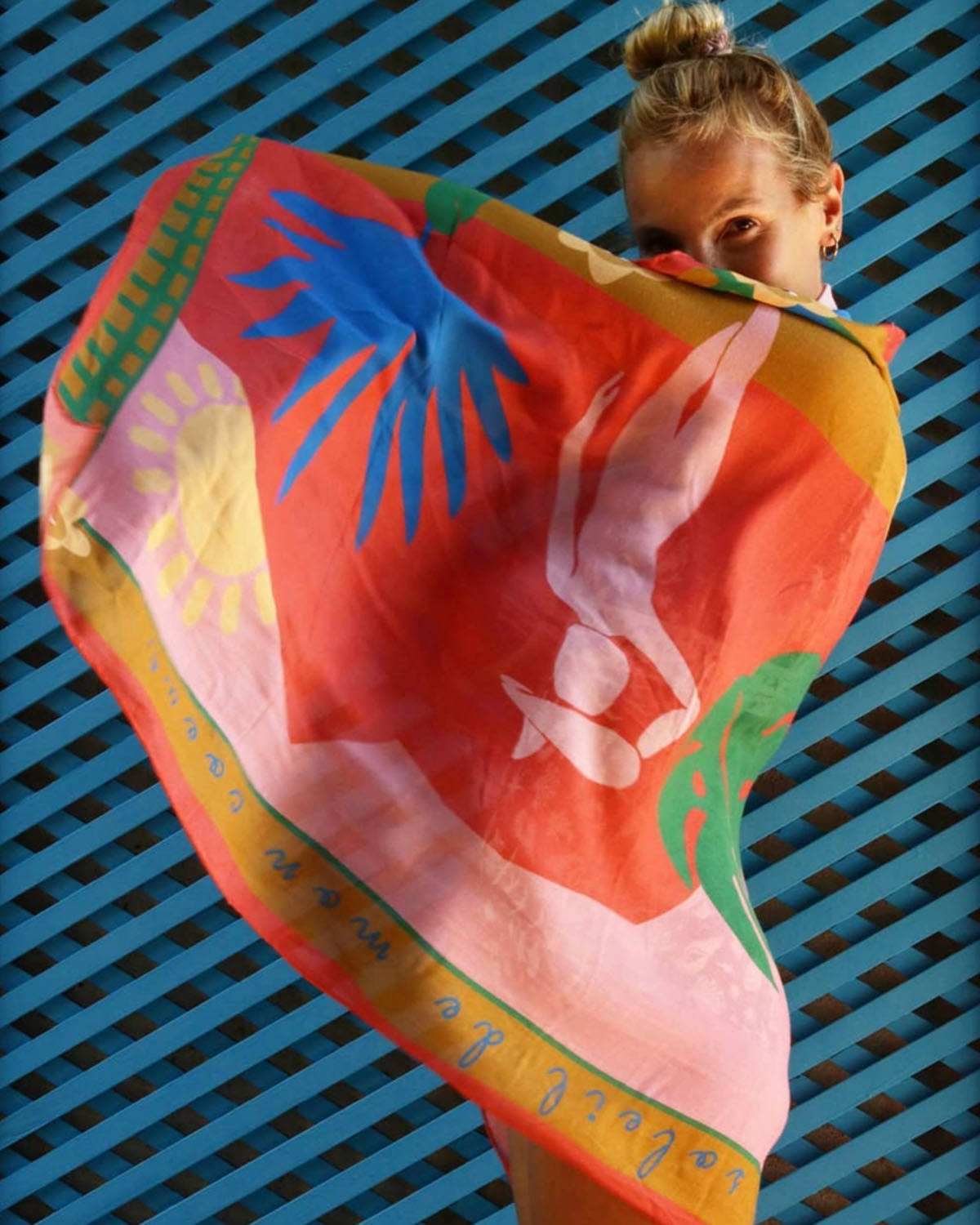 Person holding a colorful scarf with abstract designs against a blue lattice background
