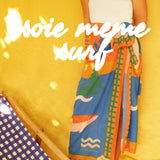 Person holding a colorful towel with 'série mème surf' text on a yellow background