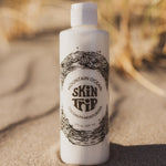 White bottle of Mountain Ocean Skin Trip product on sand with blurred natural background