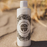 White bottle of Mountain Ocean Skin Trip product on sand with blurred natural background
