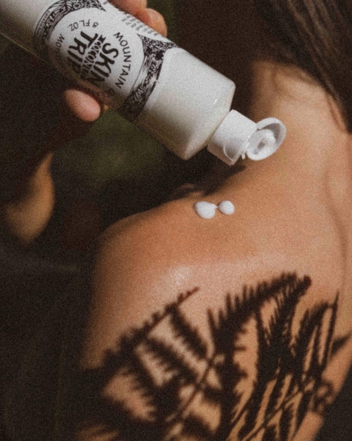 Person applying a white cream to their shoulder with a bottle labeled 'Skin So Soft'.