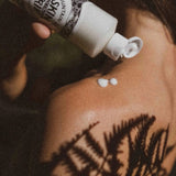 Person applying a white cream to their shoulder with a bottle labeled 'Skin So Soft'.
