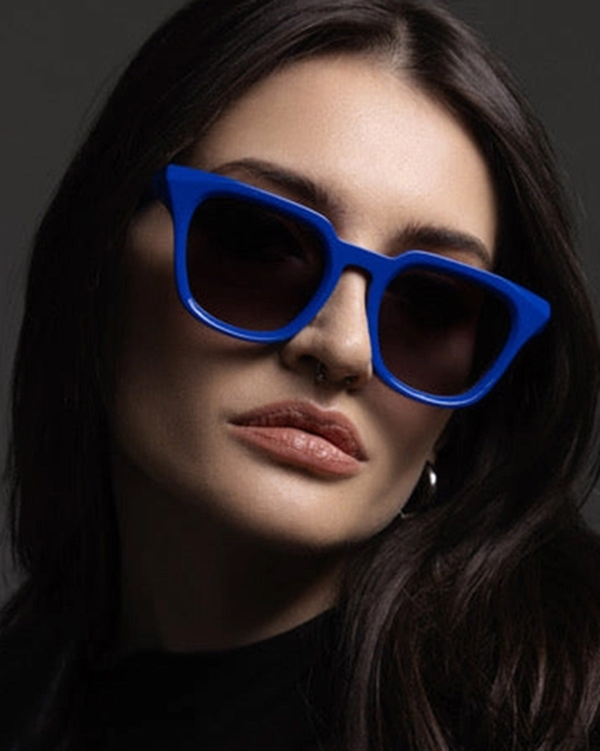 Woman wearing blue sunglasses against a dark background