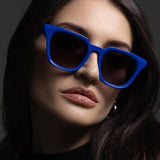 Woman wearing blue sunglasses against a dark background