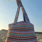 Colorful crocheted bag held by a person on a beach.