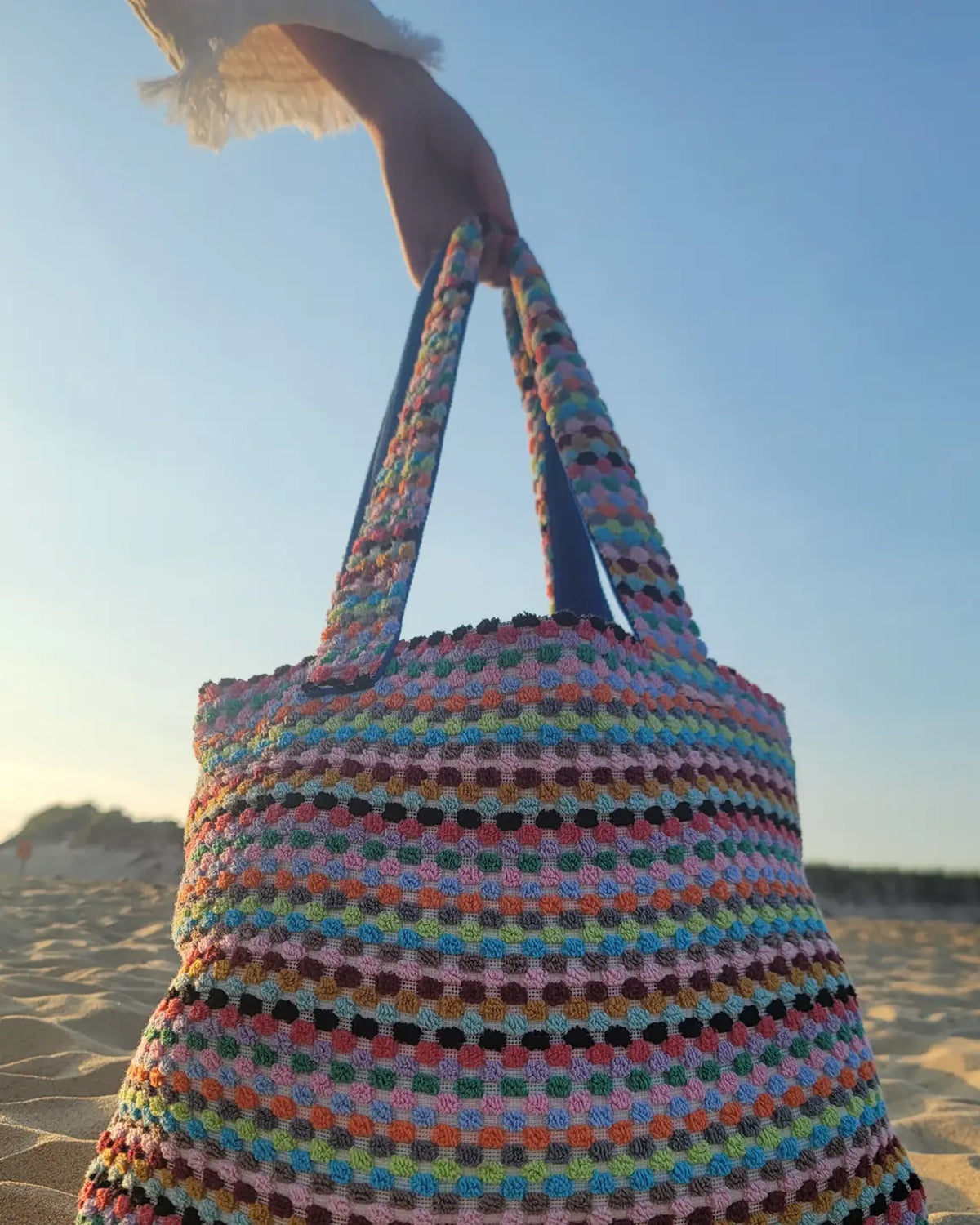 Colorful crocheted bag held by a person on a beach.