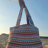 Colorful crocheted bag held by a person on a beach.