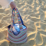 Colorful woven bag held by a hand on sandy ground