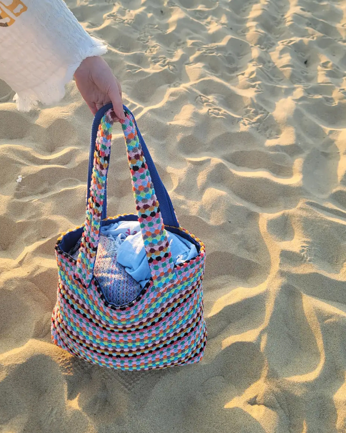 Colorful woven bag held by a hand on sandy ground