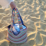 Colorful woven bag held by a hand on sandy ground