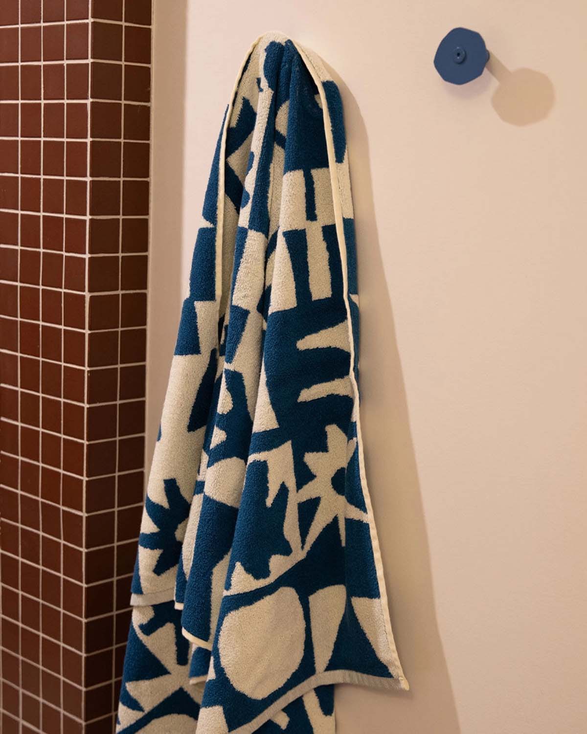 Blue and white patterned towel hanging on a hook against a tiled bathroom wall
