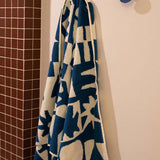 Blue and white patterned towel hanging on a hook against a tiled bathroom wall